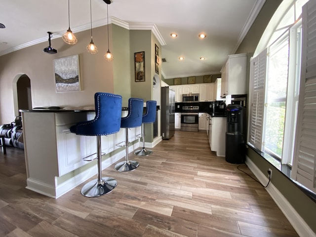 kitchen featuring white cabinets, ornamental molding, decorative light fixtures, a kitchen bar, and stainless steel appliances