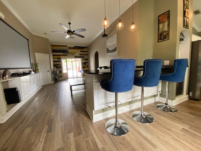 bar featuring ceiling fan, crown molding, hanging light fixtures, light hardwood / wood-style floors, and fridge