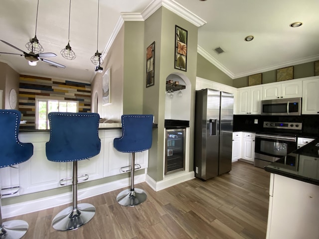 kitchen featuring ornamental molding, stainless steel appliances, beverage cooler, white cabinetry, and hanging light fixtures