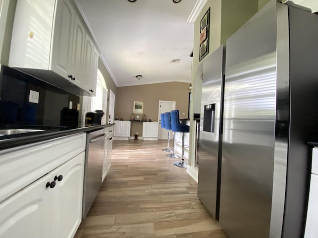 kitchen with vaulted ceiling, light wood-type flooring, ornamental molding, white cabinetry, and stainless steel appliances