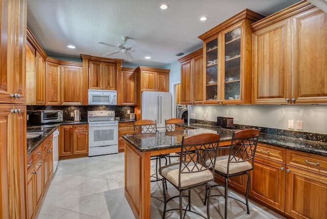 kitchen with a center island, white appliances, dark stone counters, a textured ceiling, and a breakfast bar area