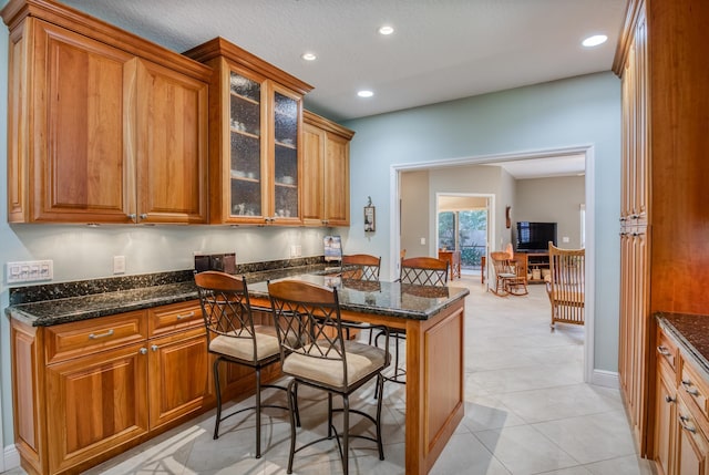 kitchen featuring kitchen peninsula, a kitchen breakfast bar, light tile patterned floors, and dark stone countertops