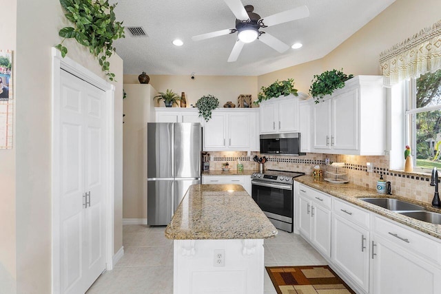 kitchen with sink, stainless steel appliances, a kitchen island, a textured ceiling, and light tile patterned flooring