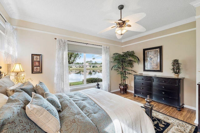 bedroom featuring a textured ceiling, ceiling fan, a water view, and crown molding