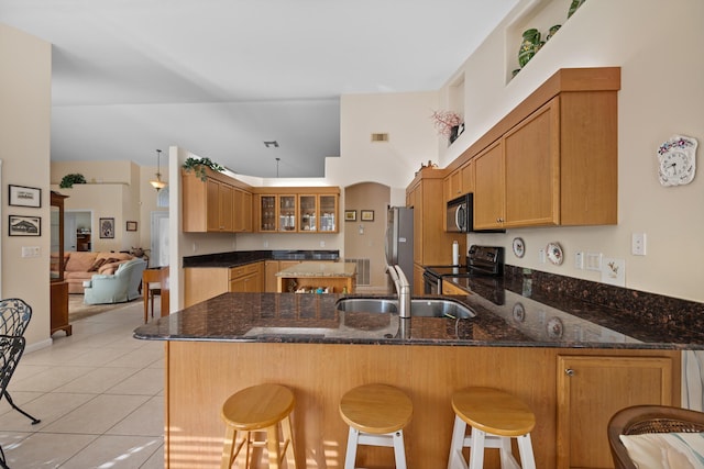 kitchen with appliances with stainless steel finishes, dark stone countertops, kitchen peninsula, and sink