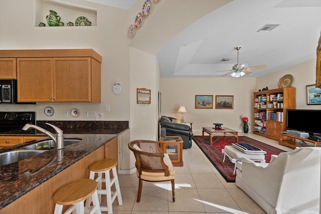 kitchen featuring light tile patterned floors, ceiling fan, a kitchen breakfast bar, dark stone countertops, and sink