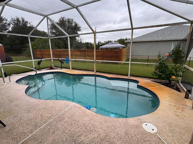 view of swimming pool with a yard, glass enclosure, and a patio