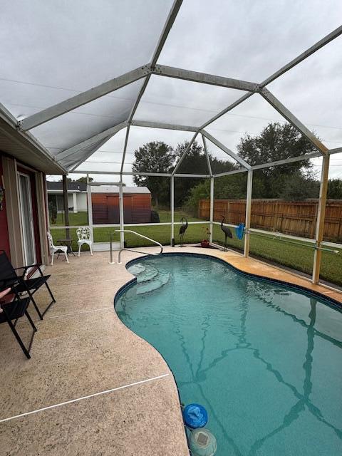 view of pool with a lawn, glass enclosure, and a patio area