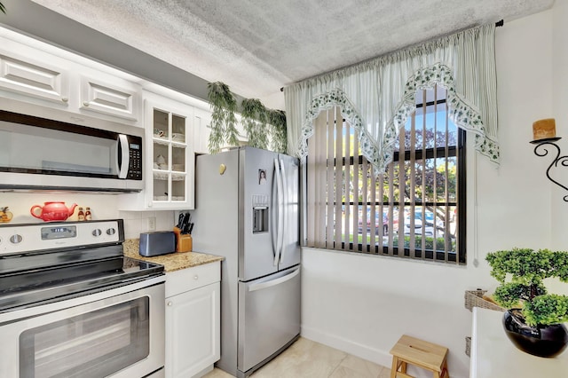 kitchen with backsplash, white cabinets, a textured ceiling, light stone counters, and stainless steel appliances