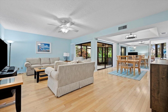 living room with ceiling fan, a textured ceiling, and light hardwood / wood-style flooring