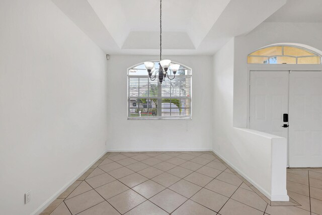 unfurnished dining area featuring a notable chandelier, light tile patterned floors, and a tray ceiling