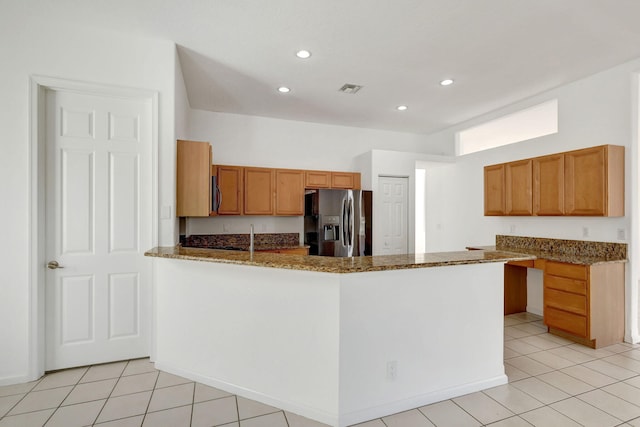 kitchen featuring kitchen peninsula, stainless steel fridge, light tile patterned floors, and dark stone counters