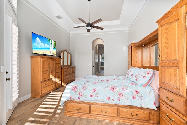 bedroom featuring ceiling fan, ornamental molding, a tray ceiling, and light hardwood / wood-style flooring