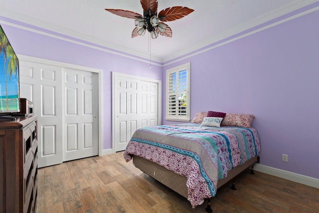 bedroom featuring hardwood / wood-style flooring, ceiling fan, ornamental molding, and two closets