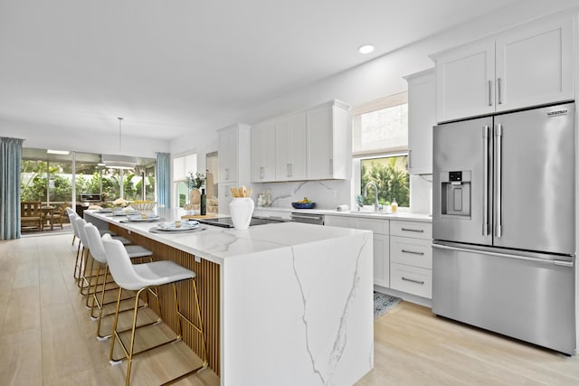 kitchen with appliances with stainless steel finishes, light stone counters, a center island, hanging light fixtures, and white cabinetry