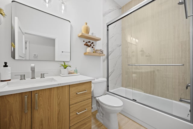 full bathroom featuring toilet, bath / shower combo with glass door, wood finished floors, and vanity