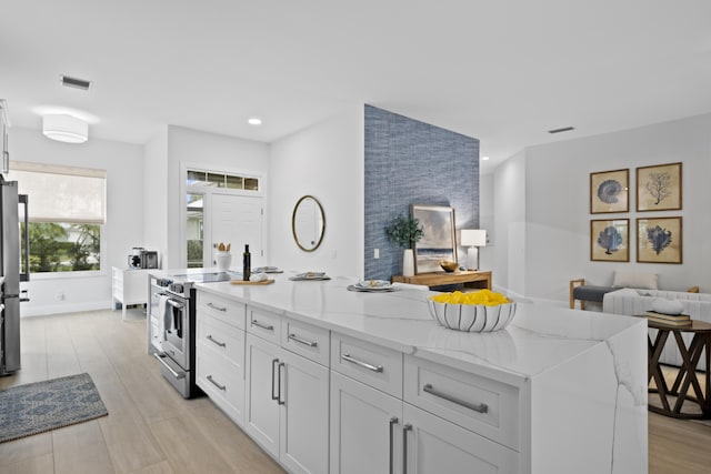 kitchen with light stone counters, a kitchen island with sink, white cabinets, appliances with stainless steel finishes, and light wood finished floors