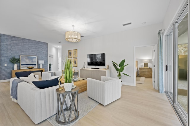 living area with a chandelier, an accent wall, visible vents, baseboards, and light wood-type flooring