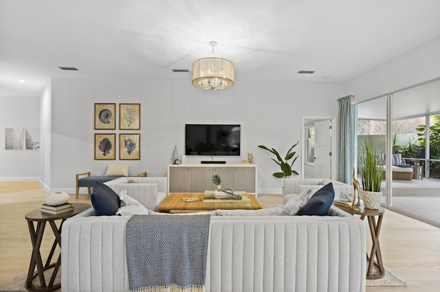 living room featuring light wood-style floors, baseboards, visible vents, and a notable chandelier