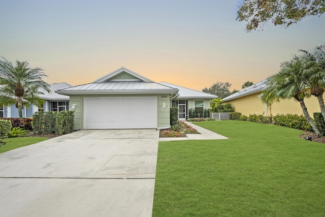 ranch-style house with driveway, metal roof, an attached garage, a standing seam roof, and a yard