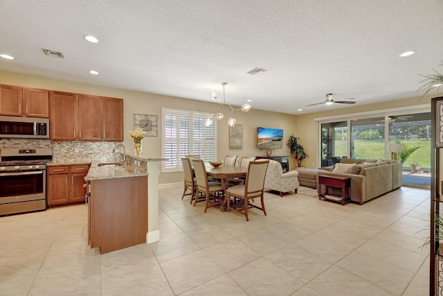 kitchen featuring pendant lighting, ceiling fan, light stone countertops, tasteful backsplash, and stainless steel appliances