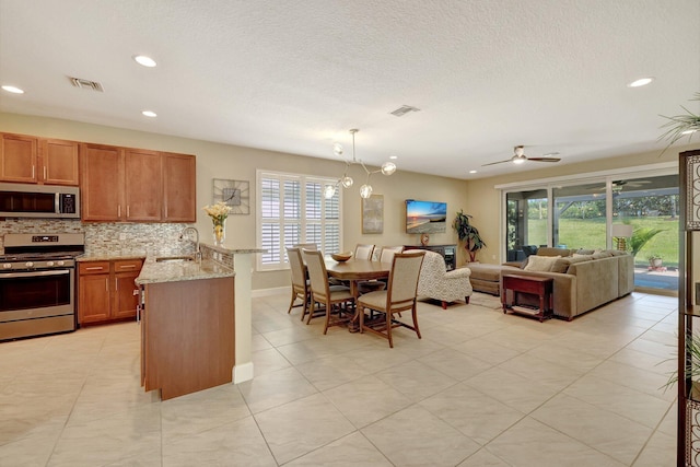 kitchen with decorative backsplash, light stone counters, stainless steel appliances, ceiling fan, and sink