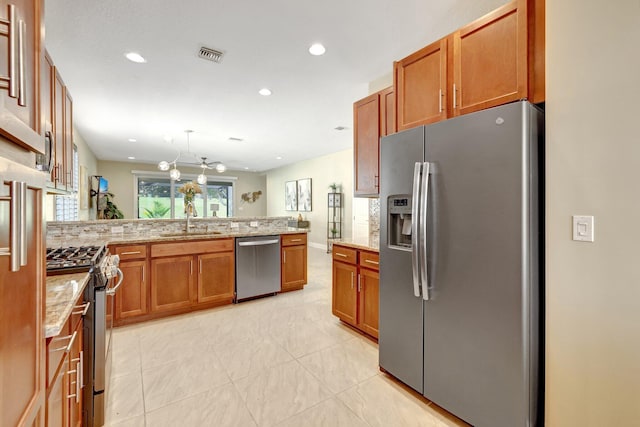 kitchen featuring kitchen peninsula, appliances with stainless steel finishes, backsplash, light stone counters, and sink