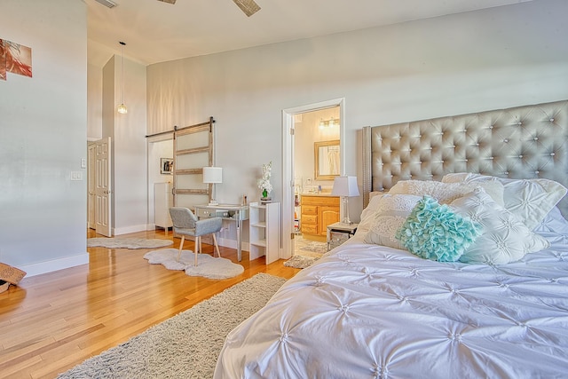 bedroom featuring connected bathroom, hardwood / wood-style flooring, a barn door, and lofted ceiling