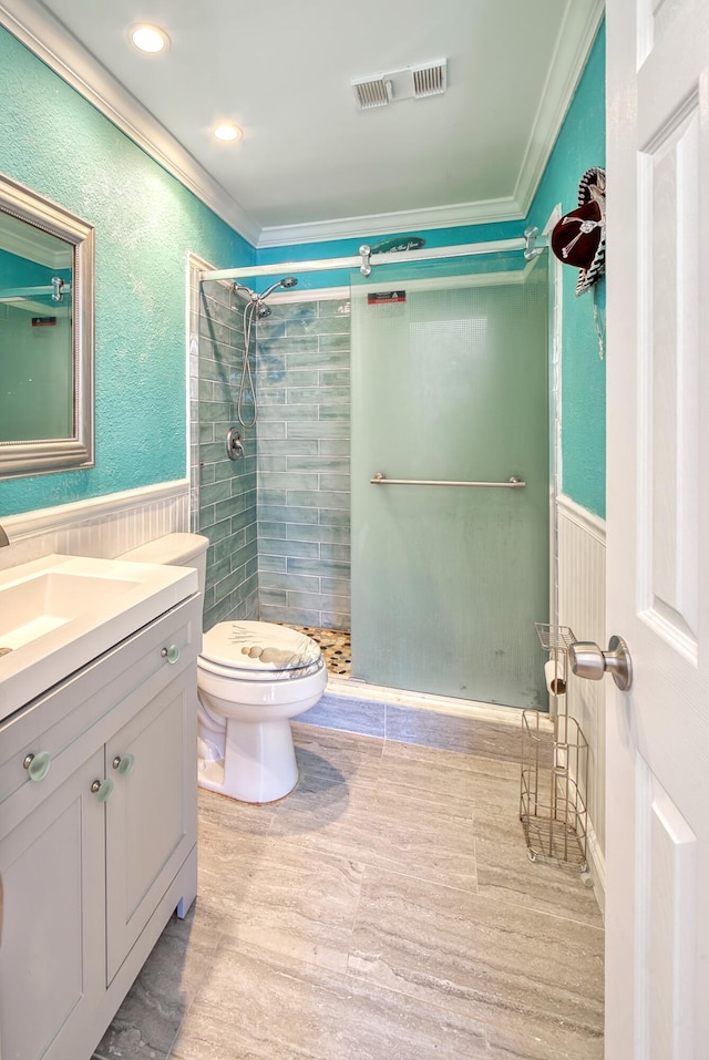 bathroom with a shower with shower door, toilet, ornamental molding, and vanity