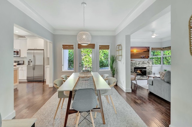 dining area with a stone fireplace, dark hardwood / wood-style floors, and ornamental molding