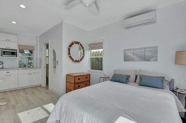 bedroom with ceiling fan, sink, a wall mounted AC, ensuite bathroom, and light hardwood / wood-style floors