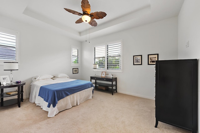 bedroom with ceiling fan, light colored carpet, and a tray ceiling