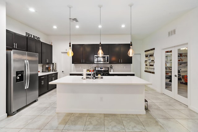 kitchen with decorative backsplash, stainless steel appliances, light tile patterned floors, decorative light fixtures, and an island with sink