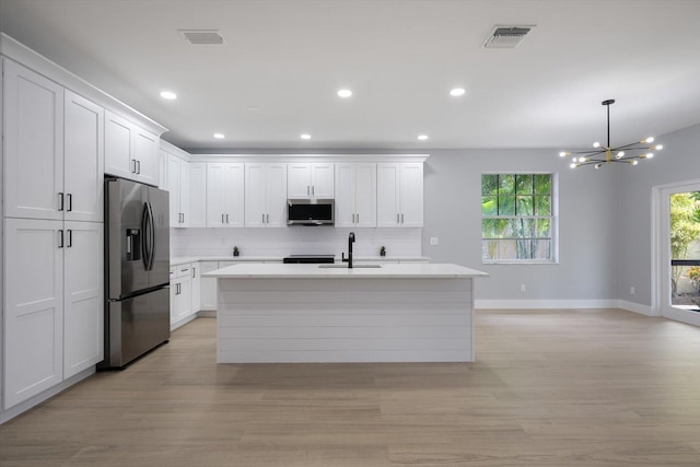 kitchen featuring backsplash, an island with sink, white cabinetry, stainless steel appliances, and a chandelier