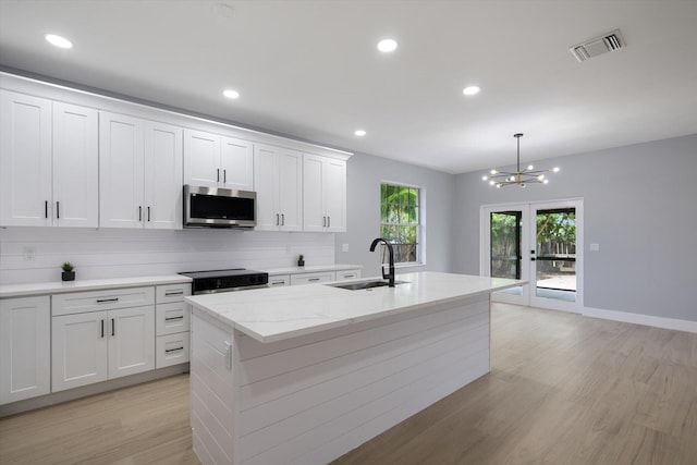 kitchen with stainless steel appliances, sink, decorative light fixtures, a center island with sink, and white cabinets