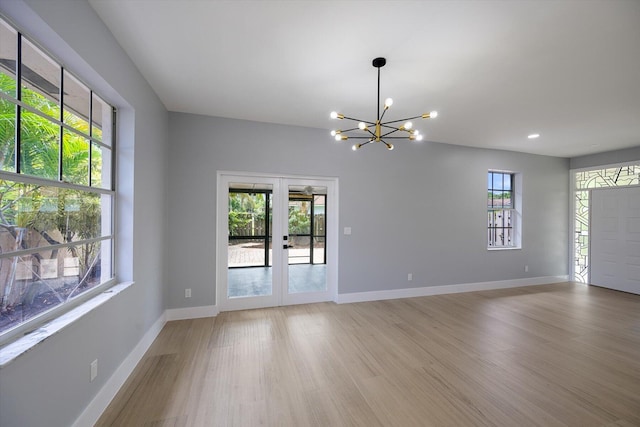 unfurnished room with french doors, light hardwood / wood-style flooring, and an inviting chandelier