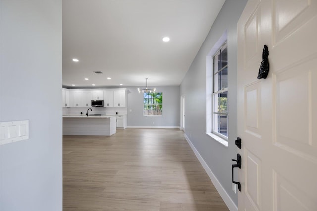 unfurnished living room featuring light hardwood / wood-style floors, an inviting chandelier, and sink