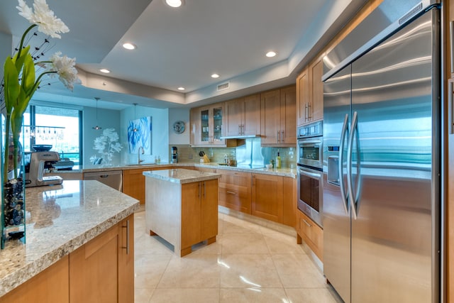 kitchen with light stone countertops, sink, pendant lighting, a kitchen island, and appliances with stainless steel finishes