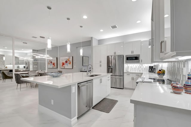 kitchen featuring white cabinetry, sink, stainless steel appliances, pendant lighting, and a center island with sink