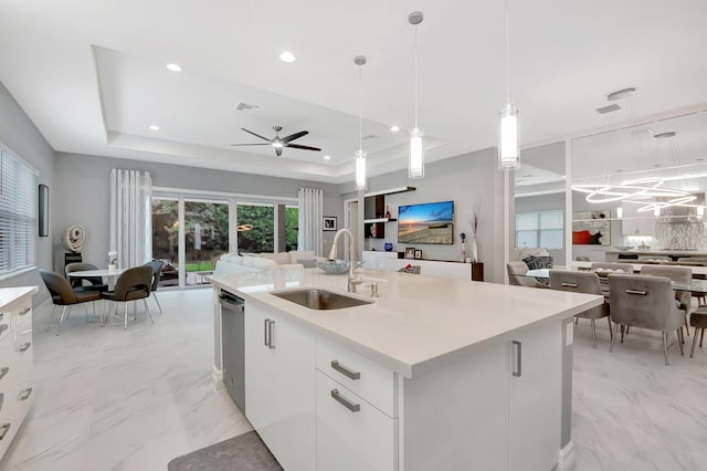 kitchen featuring pendant lighting, a kitchen island with sink, a raised ceiling, sink, and white cabinetry