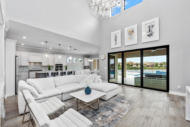 living room with a towering ceiling, light hardwood / wood-style floors, an inviting chandelier, and crown molding