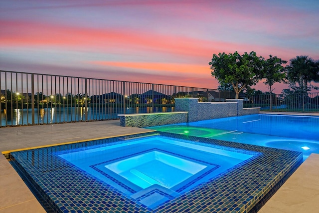 pool at dusk with an in ground hot tub and a water view