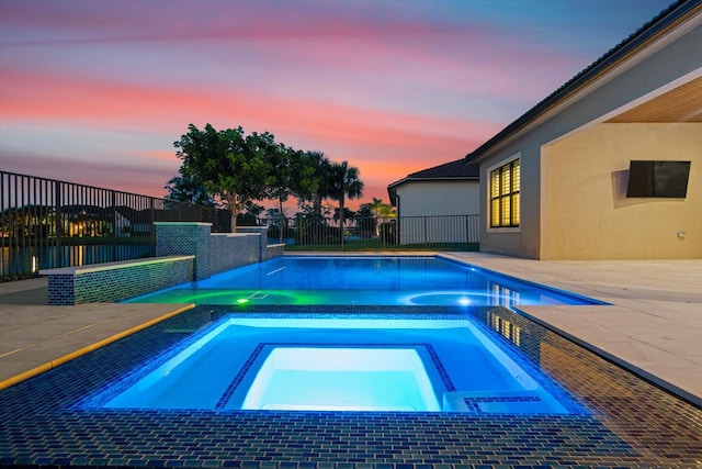 pool at dusk with an in ground hot tub and a patio area