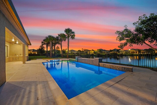 pool at dusk with a water view, an in ground hot tub, and a patio