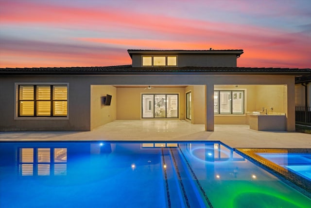 back house at dusk with area for grilling, a patio area, ceiling fan, and a pool with hot tub