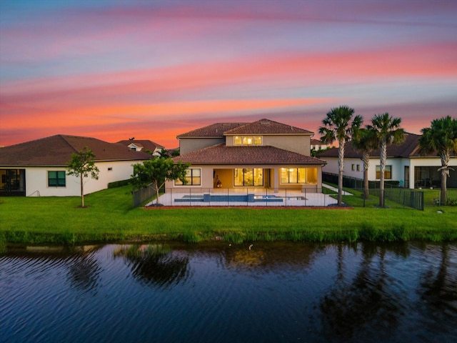 back house at dusk featuring a yard, a patio, a water view, and a swimming pool