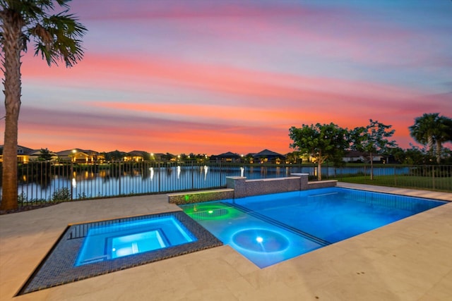 pool at dusk with a patio area, a water view, and an in ground hot tub