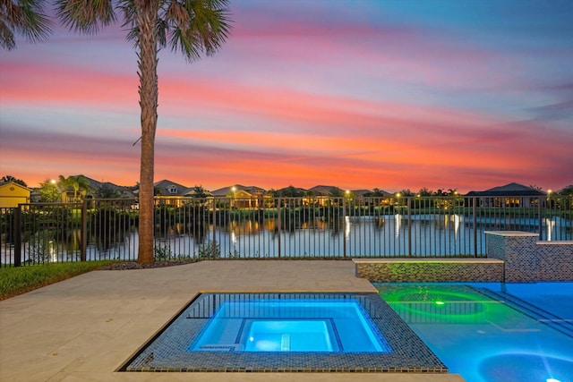 pool at dusk featuring an in ground hot tub and a water view