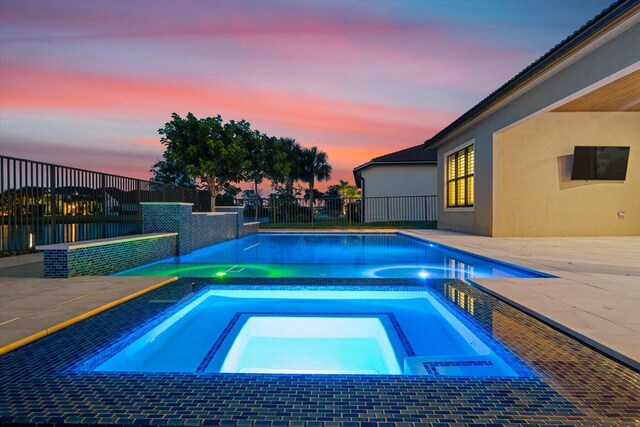 pool at dusk featuring an in ground hot tub, ceiling fan, and a patio