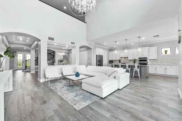 living room with crown molding, french doors, a notable chandelier, and light hardwood / wood-style flooring